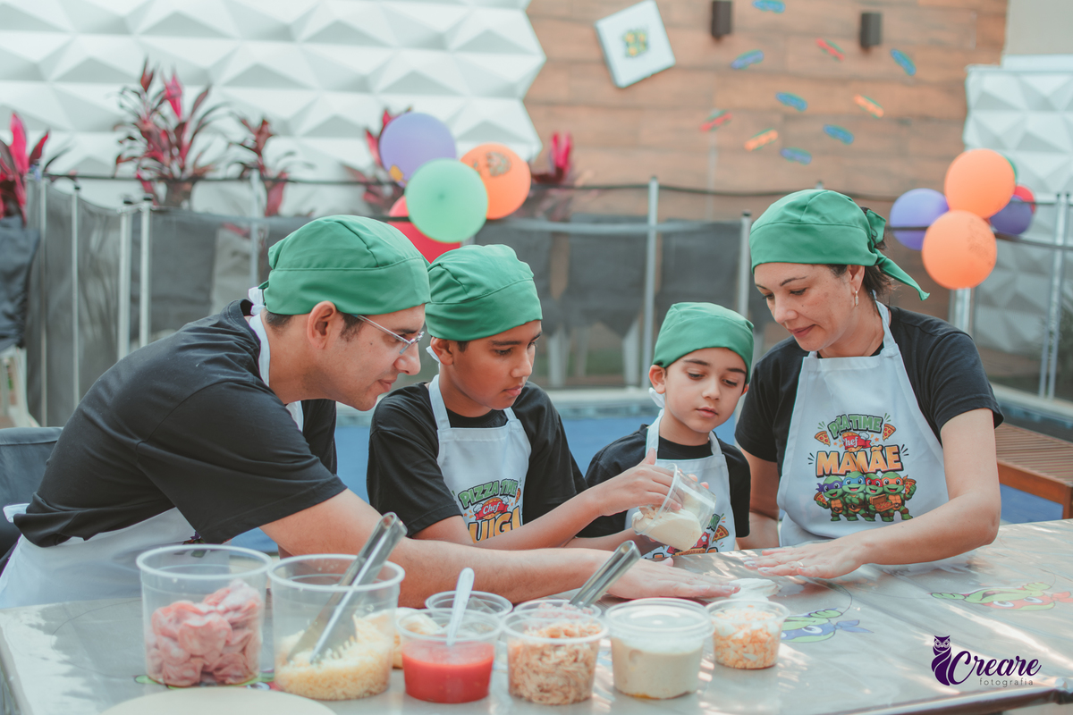 Uma familia, com dois meninos, pai e mãe, preparando pizza, durante festa de aniversário infantil em casa.