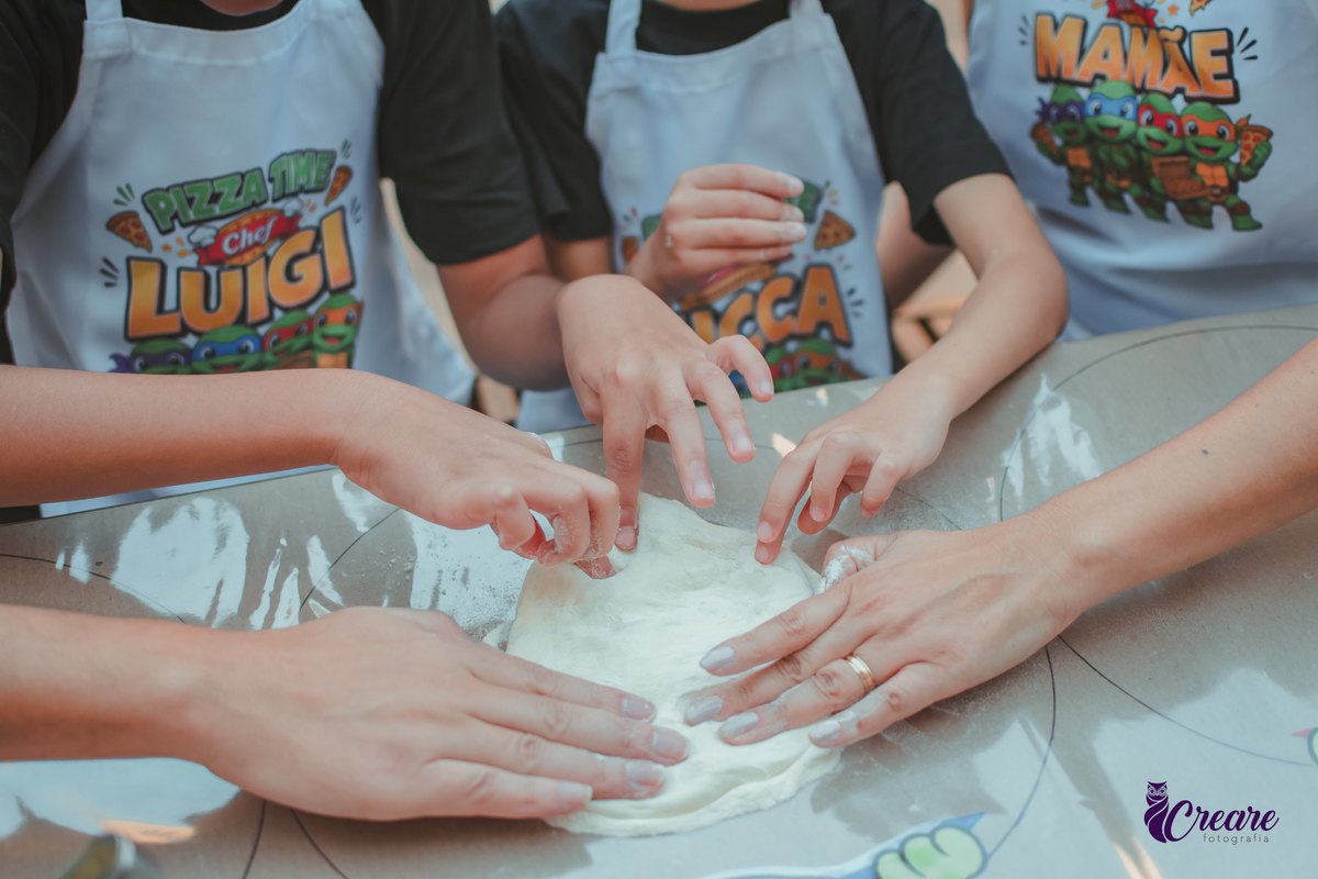 detalhes das mãos de uma familia, com dois meninos, pai e mãe, preparando pizza, durante festa de aniversário infantil em casa.