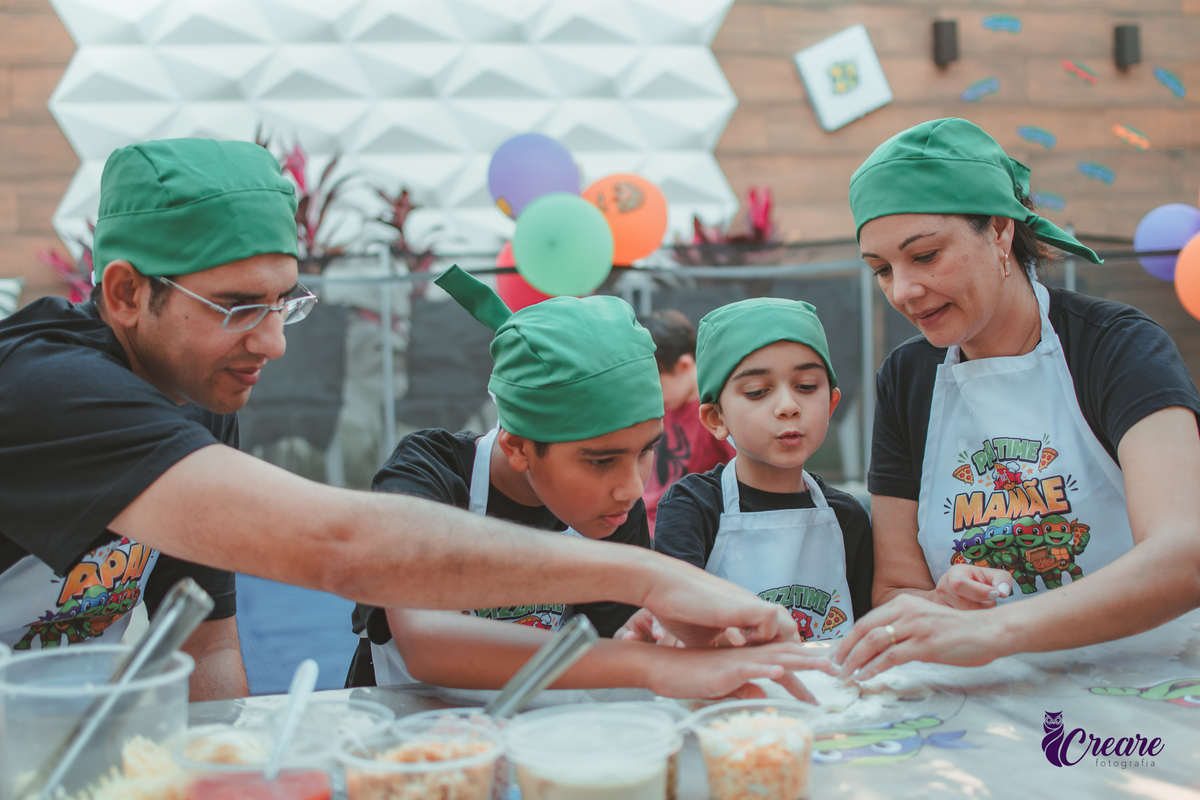 Uma familia, com dois meninos, pai e mãe, preparando pizza, durante festa de aniversário infantil em casa.