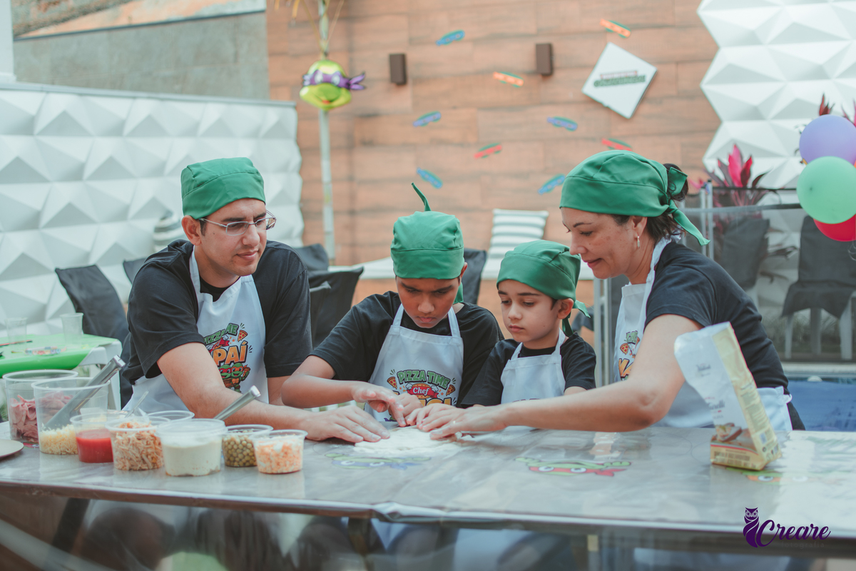 Uma familia, com dois meninos, pai e mãe, preparando pizza, durante festa de aniversário infantil em casa.
