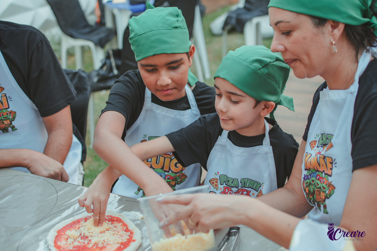 Uma familia, com dois meninos, pai e mãe, preparando pizza, durante festa de aniversário infantil em casa.