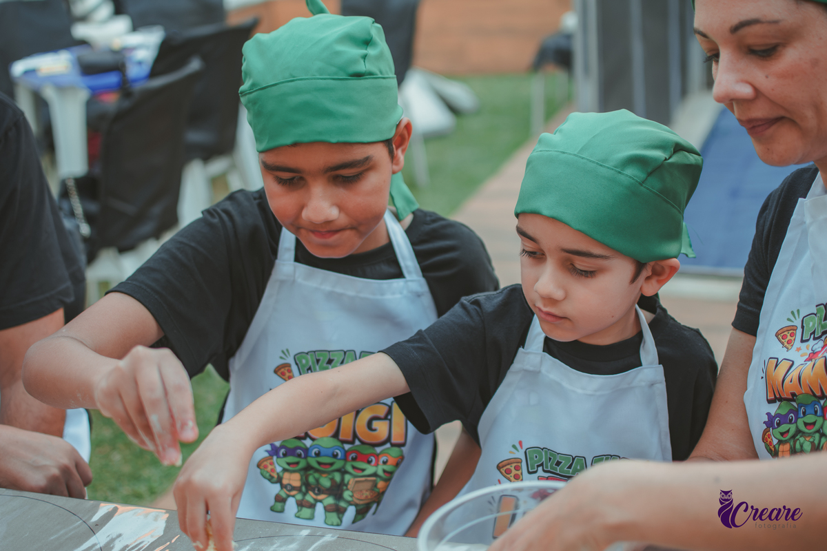 Uma familia, com dois meninos, pai e mãe, preparando pizza, durante festa de aniversário infantil em casa.