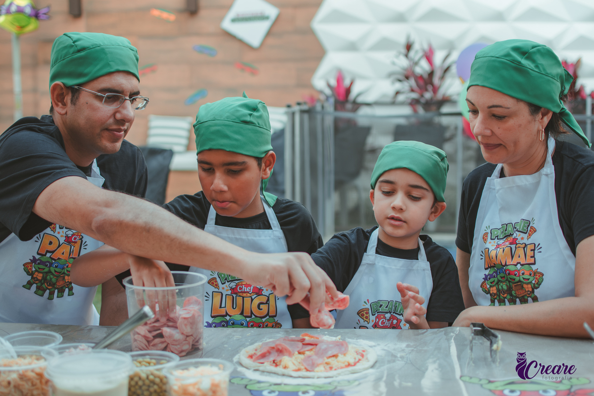Uma familia, com dois meninos, pai e mãe, preparando pizza, durante festa de aniversário infantil em casa.