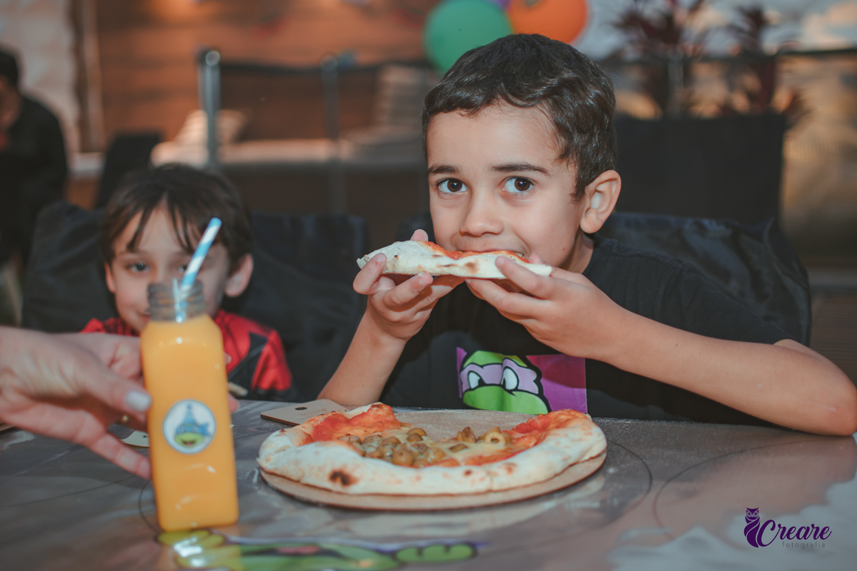 uma criança comendo a pizza que produziu na oficina de pizza, durante sua festa de aniversário em casa.