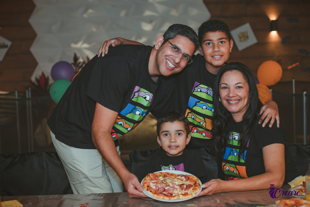 Familia com o pai, mãe e dois meninos, mostrando a pizza que produziram durante festa infantil em casa.