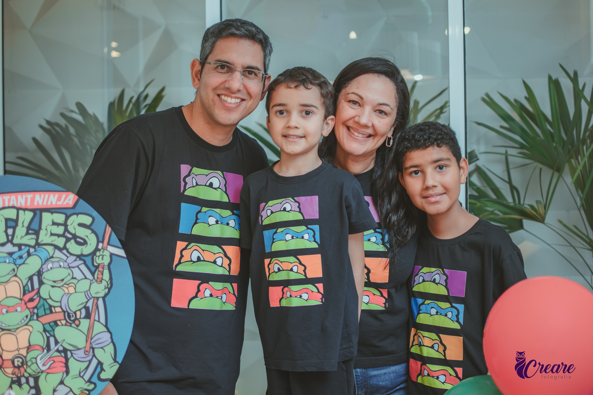 Uma família em frente a decoração do aniversário de 6 anos com tema tartarugas ninjas.