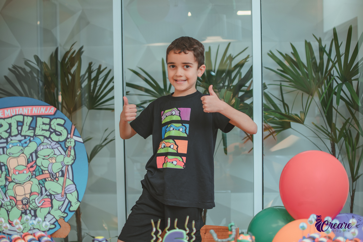 Um menino em frente a decoração do seu aniversário de 6 anos com tema tartarugas ninjas.