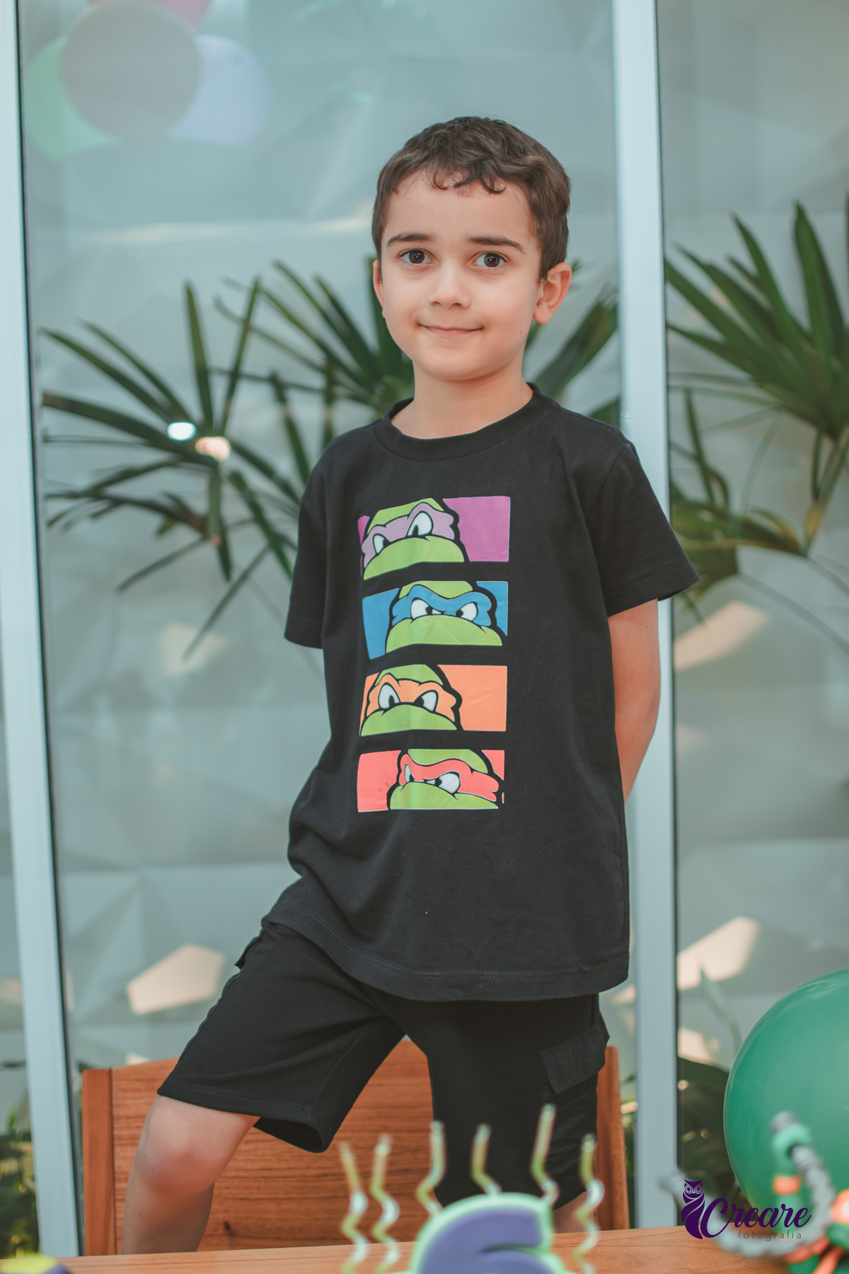 Um menino em frente a decoração do seu aniversário de 6 anos com tema tartarugas ninjas.