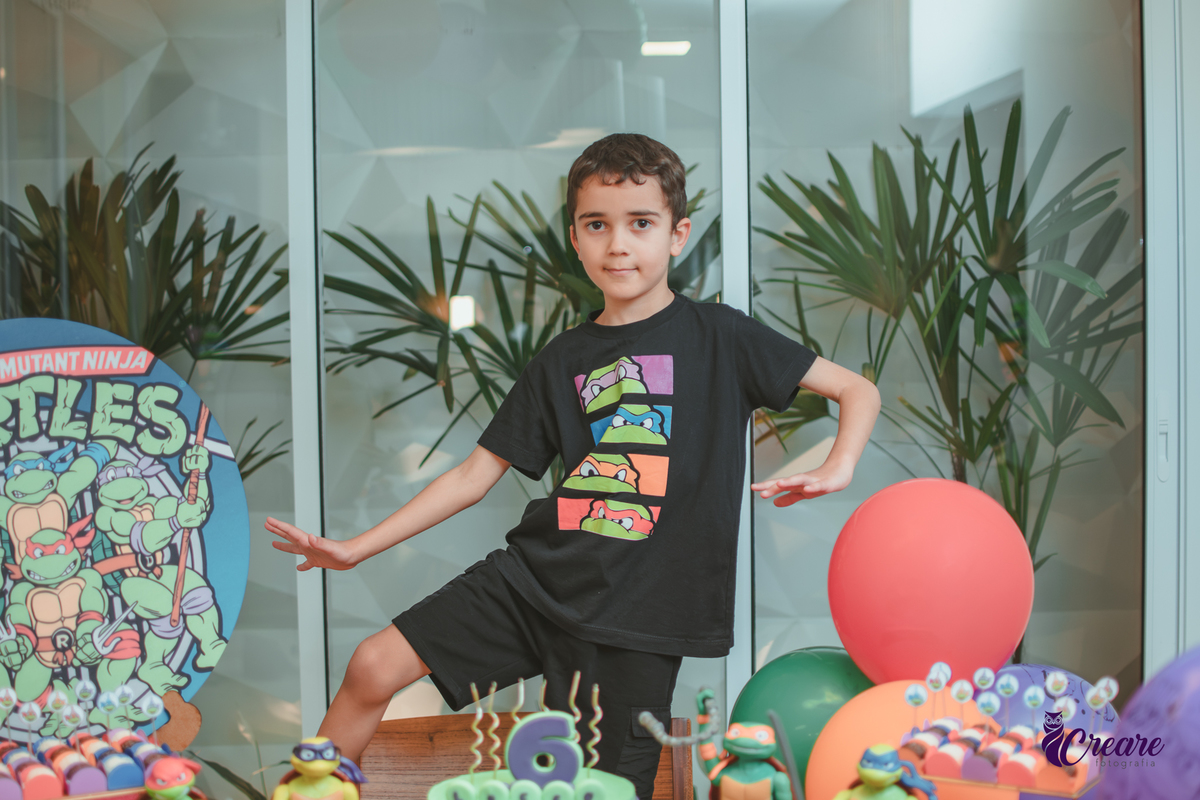 Um menino em frente a decoração do seu aniversário de 6 anos com tema tartarugas ninjas.
