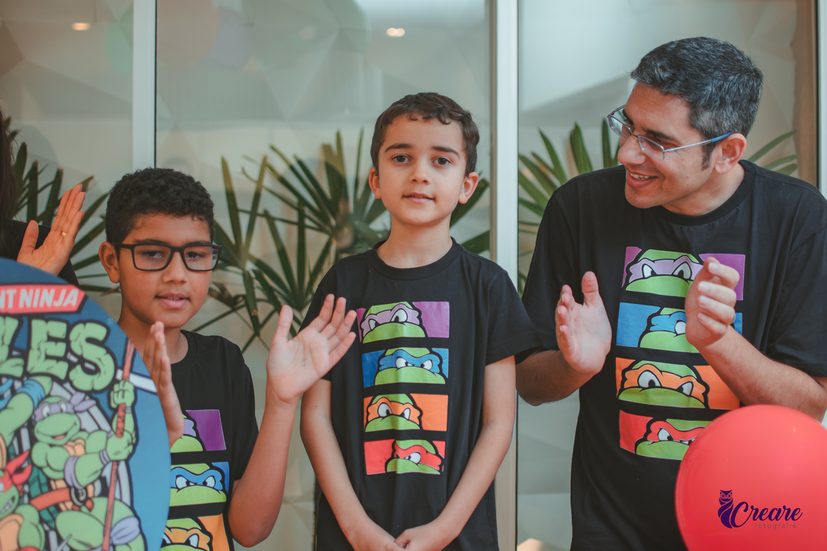 Uma família com pais, mãe e dois meninos, cantando parabéns para o menino de 6 anos, durante aniversário infantil.