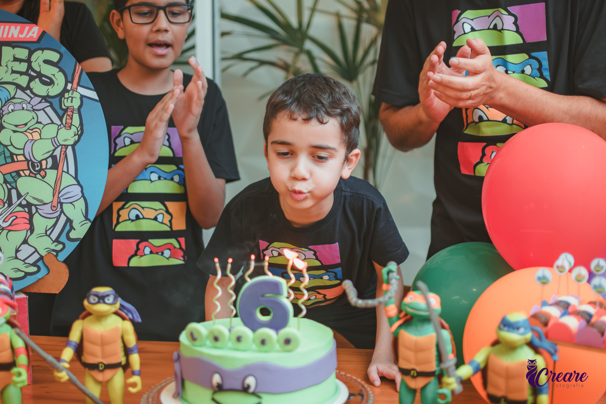 Um menino soprando as velas de 6 anos do seu aniversário em casa.