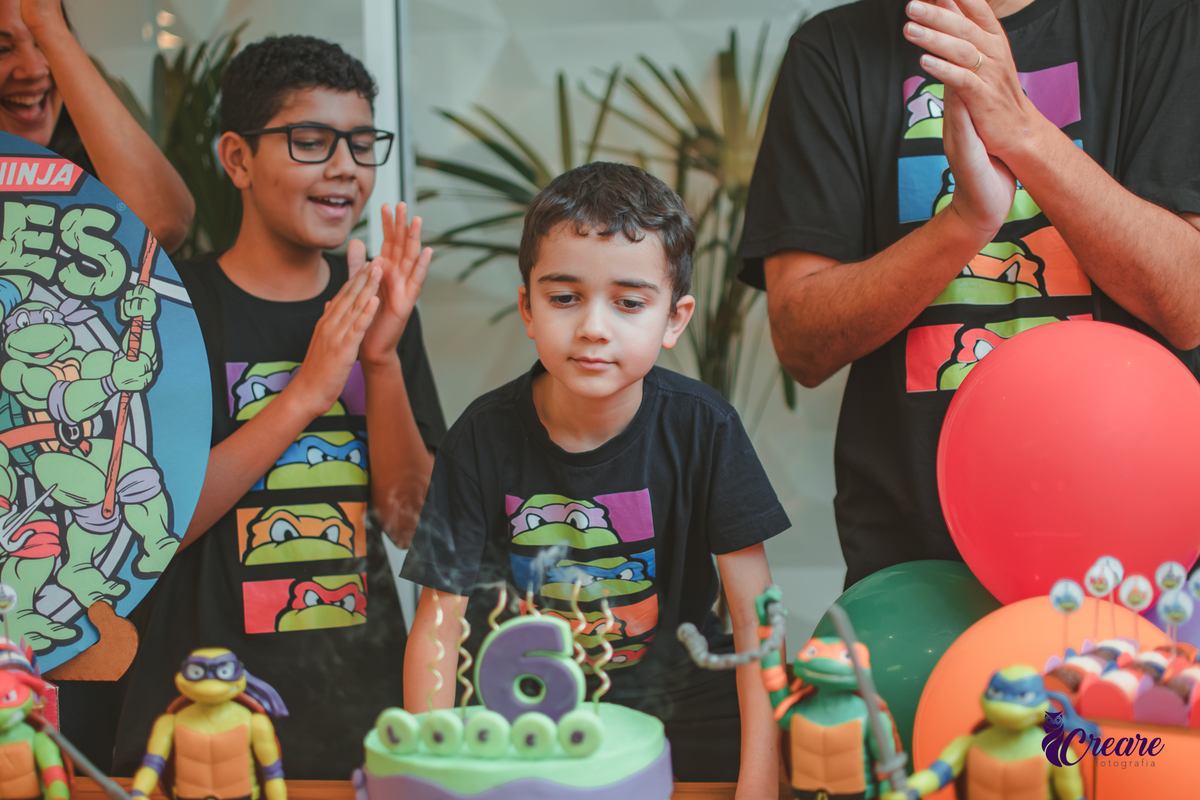 Um menino soprando as velas de 6 anos do seu aniversário em casa.