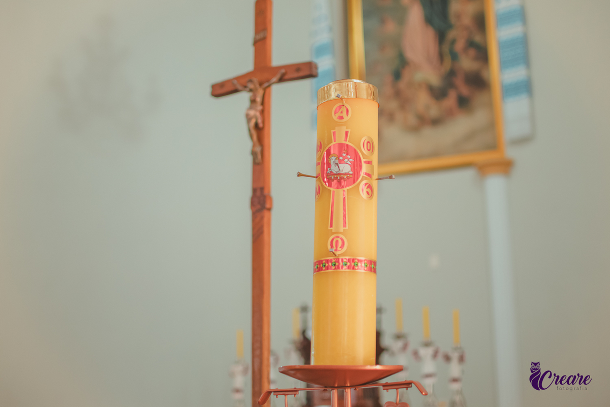 Uma vela, chamada cirio pascal, acesa e uma cruz em uma igreja preparada para um batizado infantil