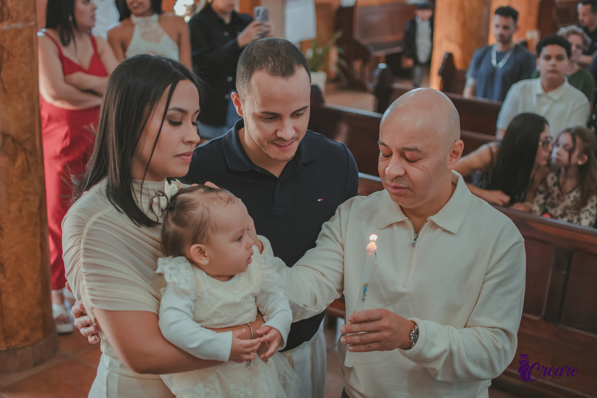 Um homem segurando uma vela de batizado ao lado do pai e mãe com o bebê no colo.