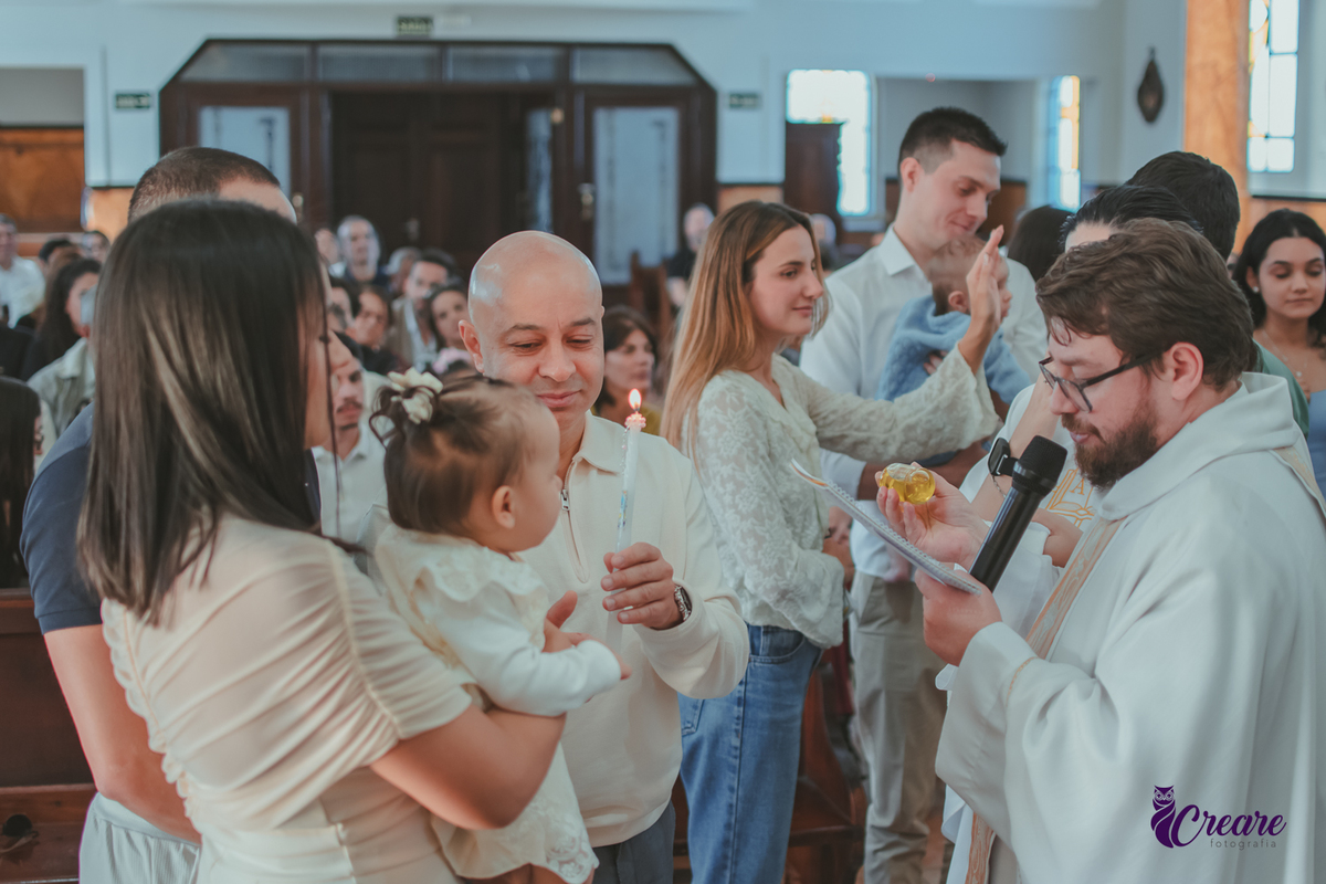 Um homem segurando uma vela de batizado ao lado do pai e mãe com o bebê no colo.