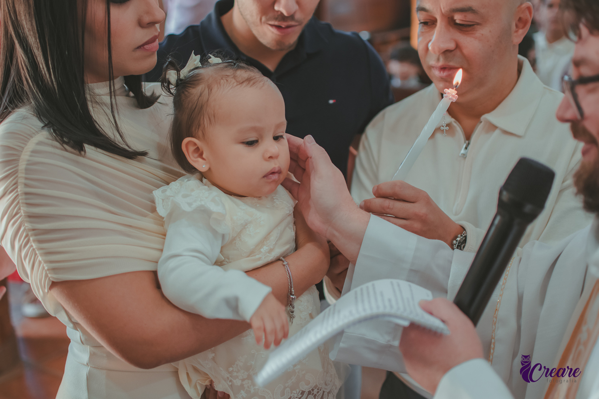 Padre ungindo os ouvidos de uma bebê, durante seu batizado na igreja Católica.