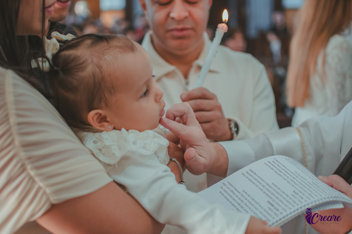 Padre ungindo a boca de uma bebê, durante seu batizado na igreja Católica.