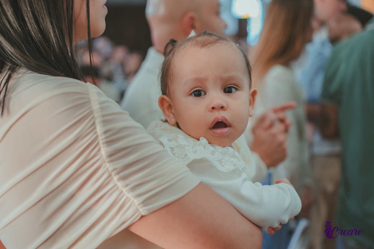 Bebê olhando para afotos, durante seu batizado.