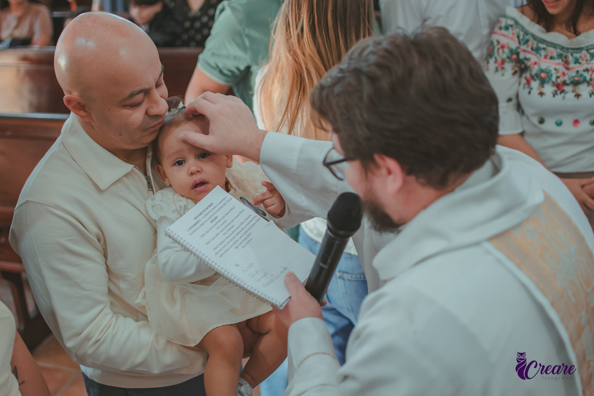 Um padre ungindo a testa de um bebê, durante batizado na igreja católica.