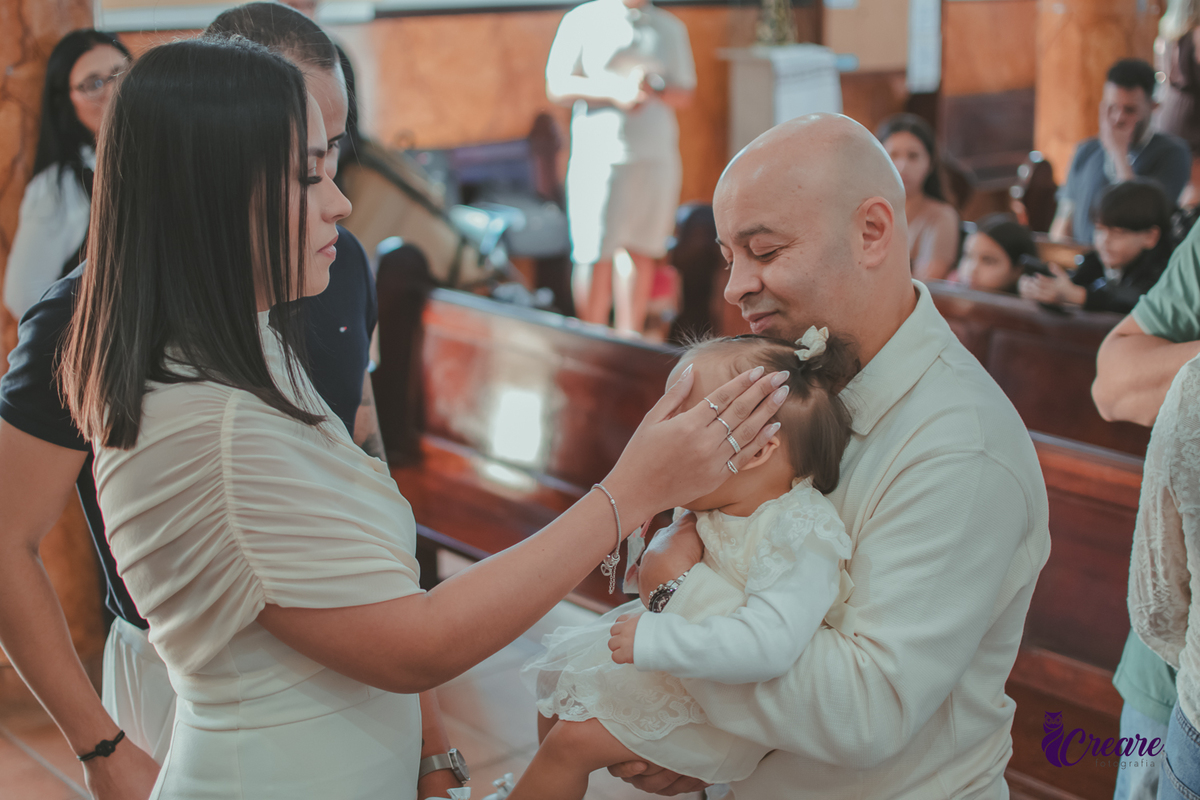 Uma mulher ungindo a testa de um bebê, durante batizado na igreja católica.