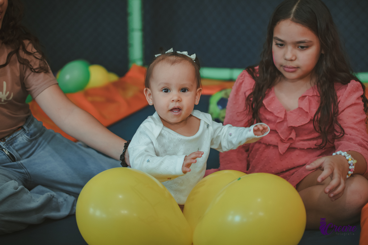 Uma bebê brincando com bolas no pula-pula, com outras crianças, durante sua festa de aniversário de 1 ano.
