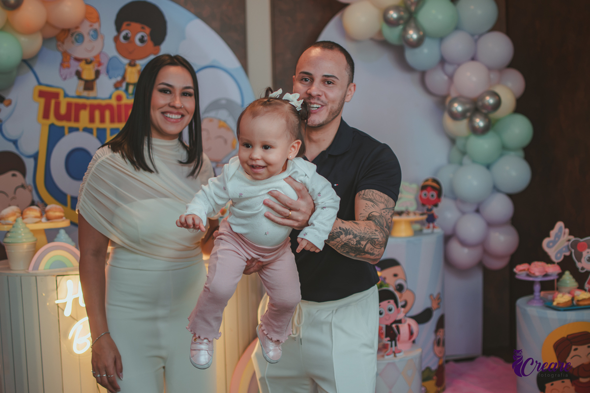Uma familia  brincando com a bebê de 1 ano em frente a mesa de decoração da festa.