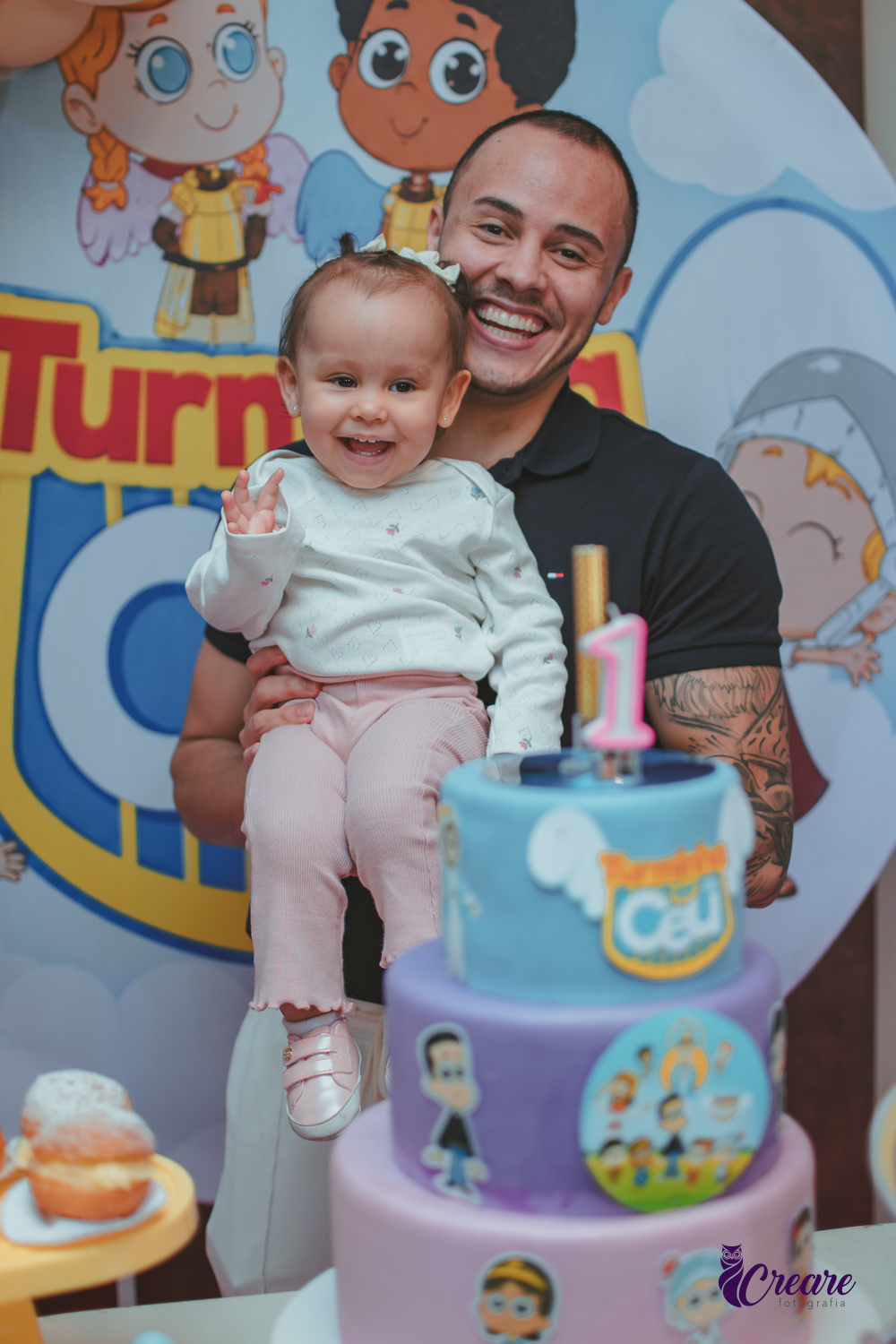 Um homem segurando bebê sorrindo no colo em frente a mesa de decoração da festa de 1 ano.