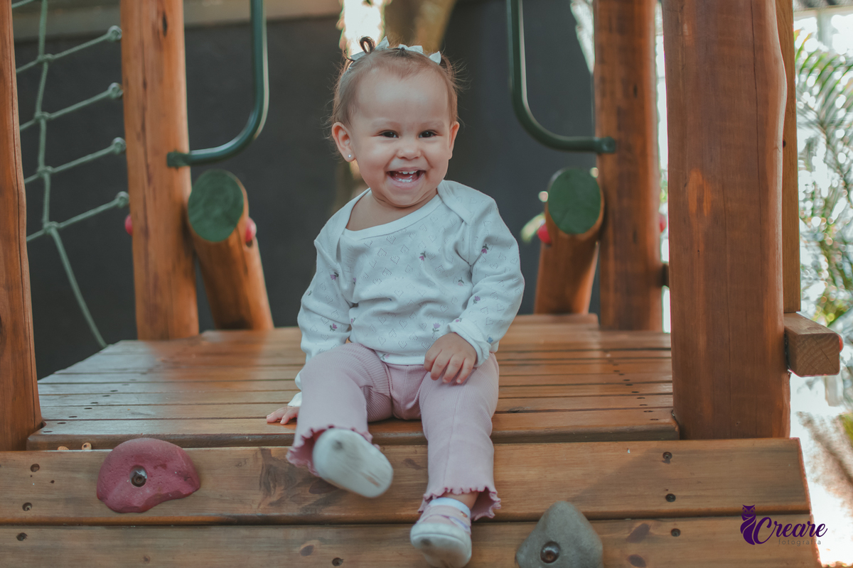 Uma criança sentada em um brinquedo de madeira e sorrindo, durante sua festa de aniversário.