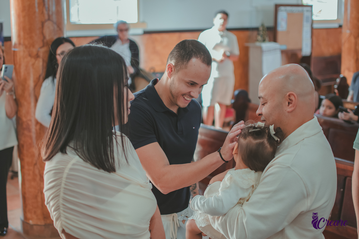 Um homem ungindo a testa de um bebê, durante batizado na igreja católica.
