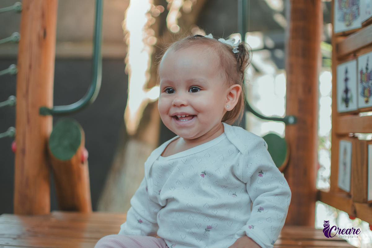 Uma criança sentada em um brinquedo de madeira e sorrindo, durante sua festa de aniversário.