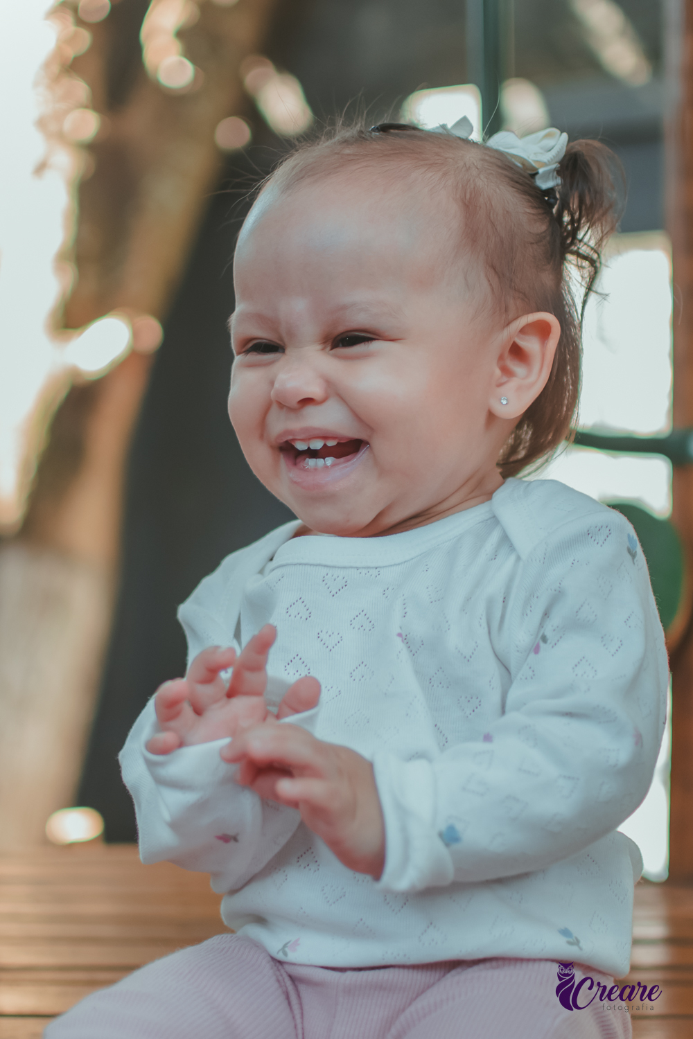 Uma criança sentada em um brinquedo de madeira e sorrindo, durante sua festa de aniversário.