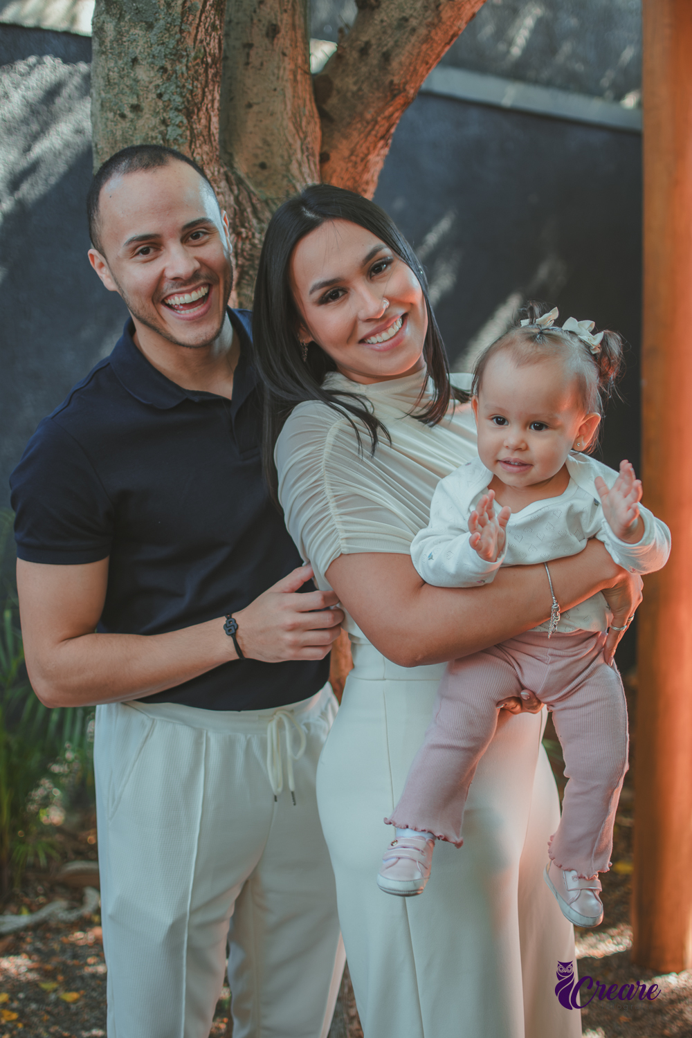 Uma família sorrindo com sua bebê de 1 ano no colo, durante festa de aniversário.