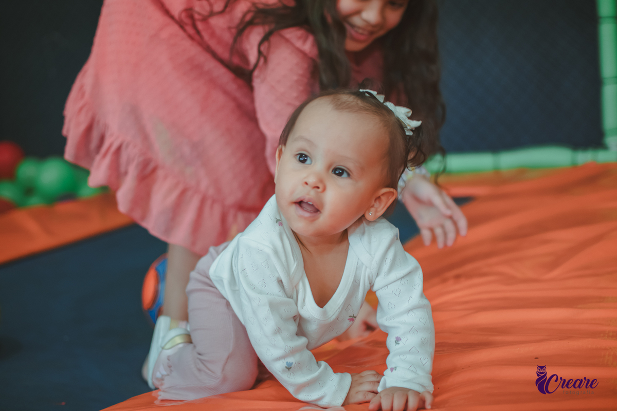 Uma bebê brincando com bolas no pula-pula, com outras crianças, durante sua festa de aniversário de 1 ano.
