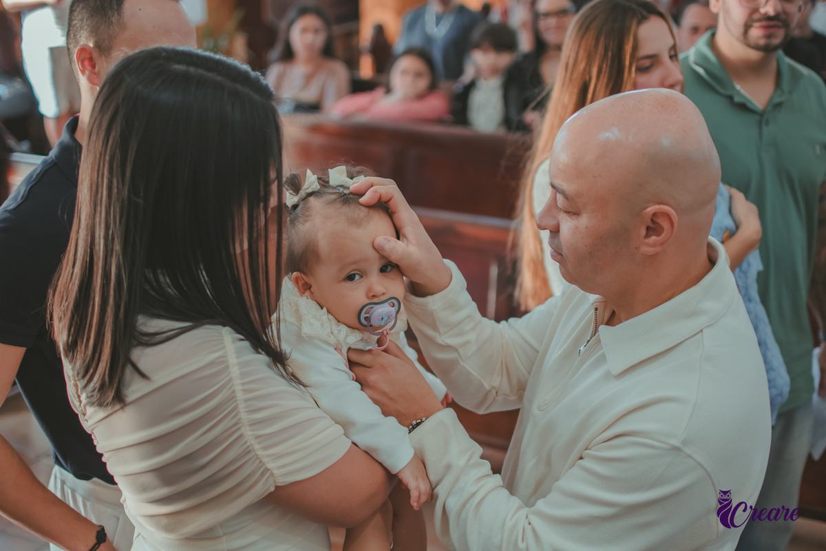 Um homem ungindo a testa de um bebê, durante batizado na igreja católica.