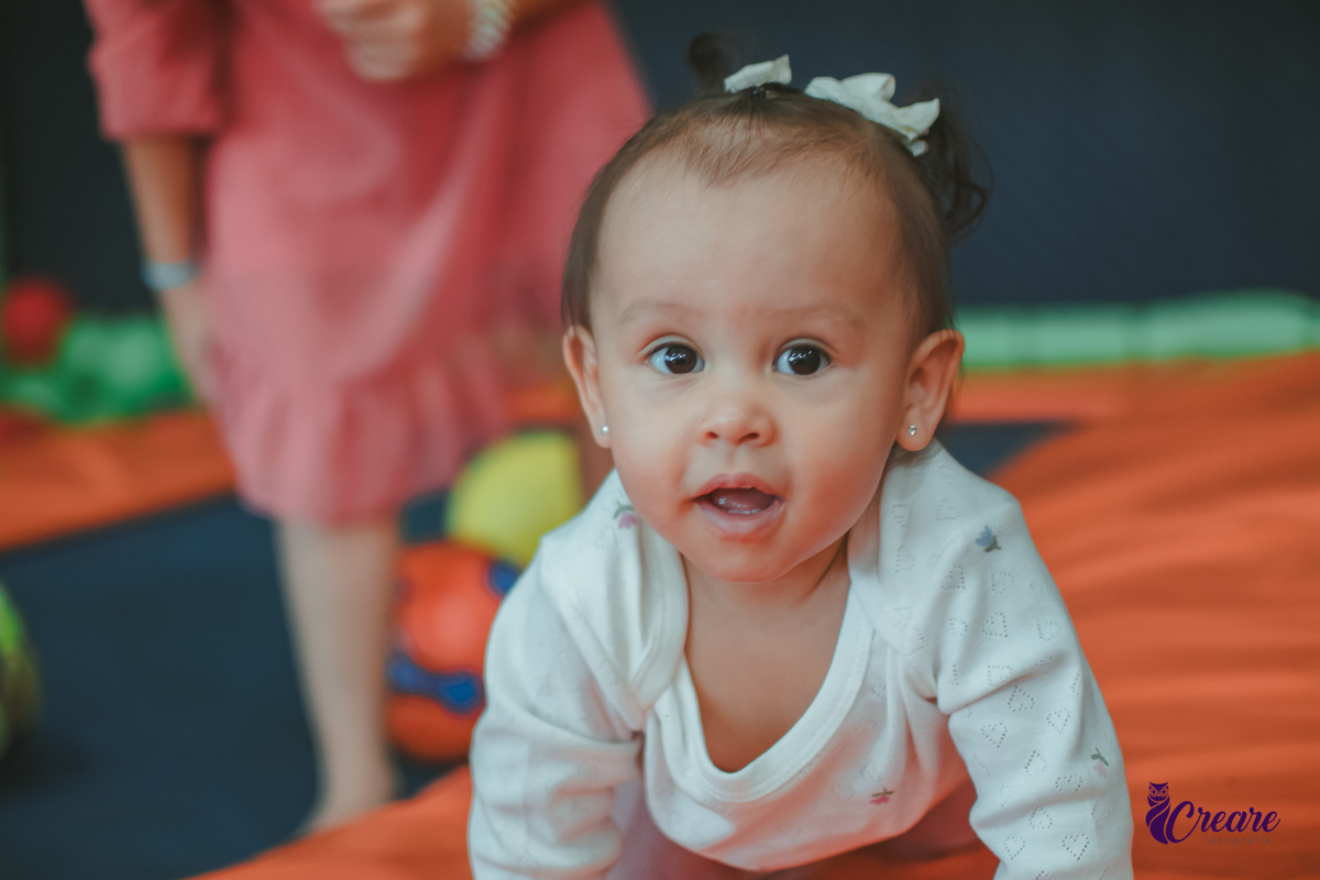 Uma bebê brincando com bolas no pula-pula, com outras crianças, durante sua festa de aniversário de 1 ano.