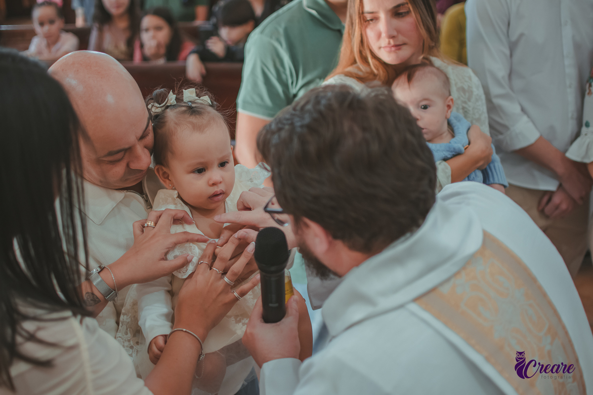 O padre ungindo o peito d euma bebê com oleo santo, durante o batizado na igreja católica.