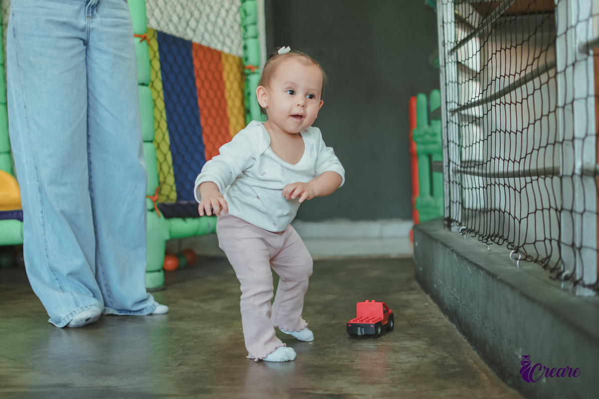 Uma bebê brincando com um carrinho vermelho, durante sua festa de aniversário de 1 ano.