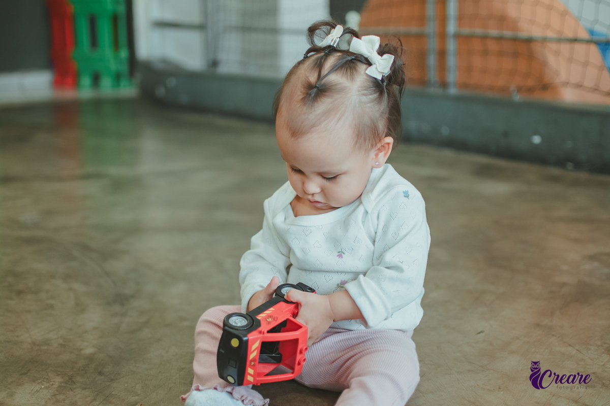 Uma bebê brincando com um carrinho vermelho, durante sua festa de aniversário de 1 ano.