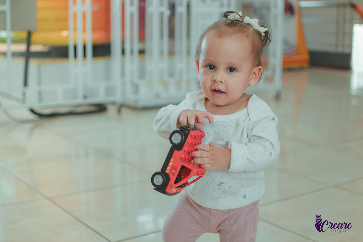 Uma bebê brincando com um carrinho vermelho, durante sua festa de aniversário de 1 ano.