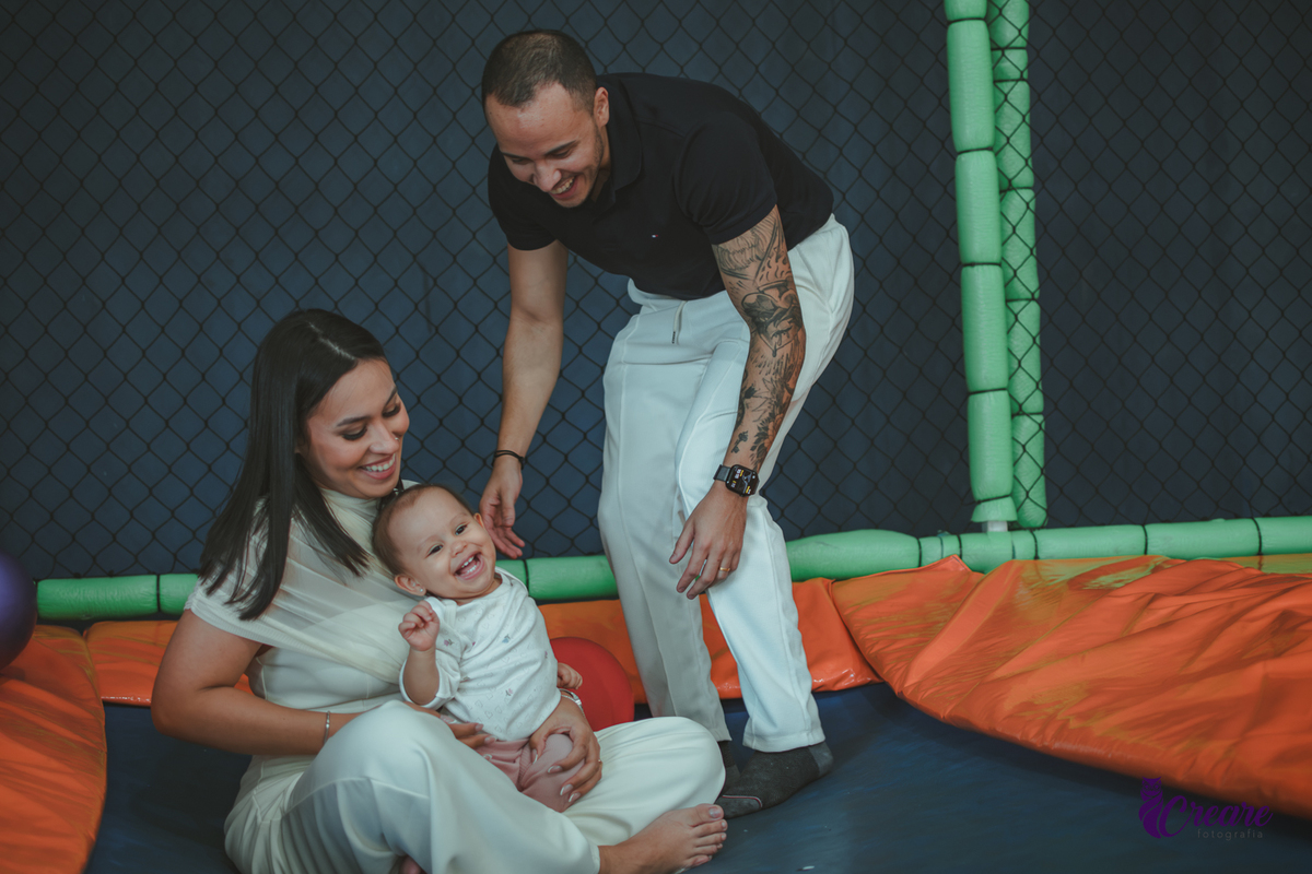 Uma bebê brincando com bolas no pula-pula, com seus pais, durante sua festa de aniversário de 1 ano.
