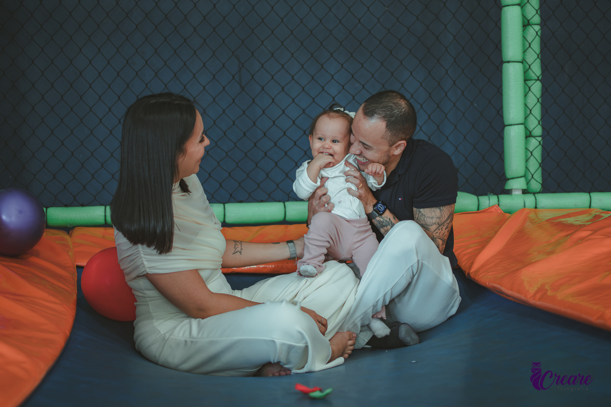 Uma bebê brincando com bolas no pula-pula, com seus pais, durante sua festa de aniversário de 1 ano.
