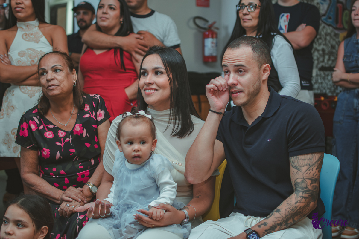 Uma família assistindo a retospectiva e o pai emocionado, durante festa de aniversário de 1 ano.
