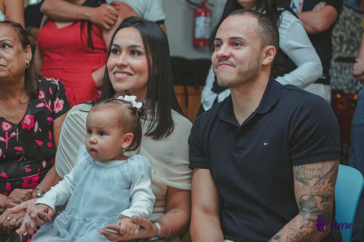 Uma família assistindo a retospectiva e o pai emocionado, durante festa de aniversário de 1 ano.