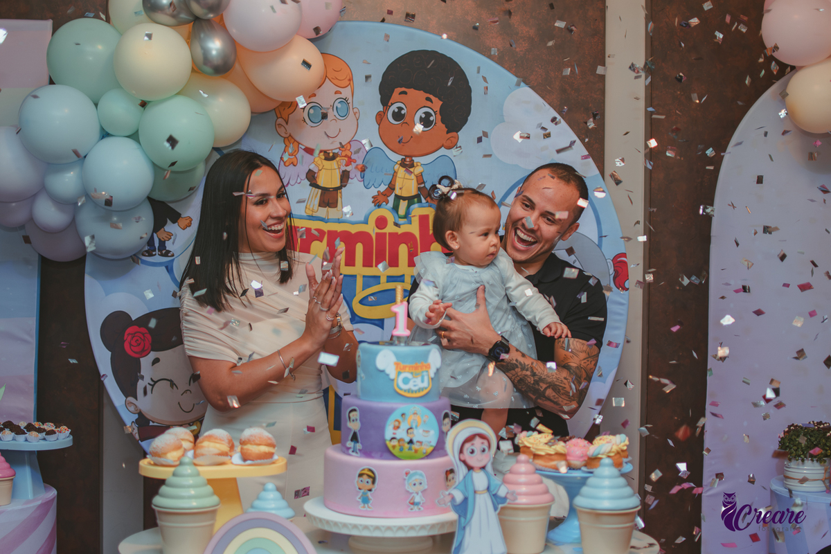 Uma família cantando parabéns enquanto papeis brilhantes caem, durante festa de aniversário de 1 ano.