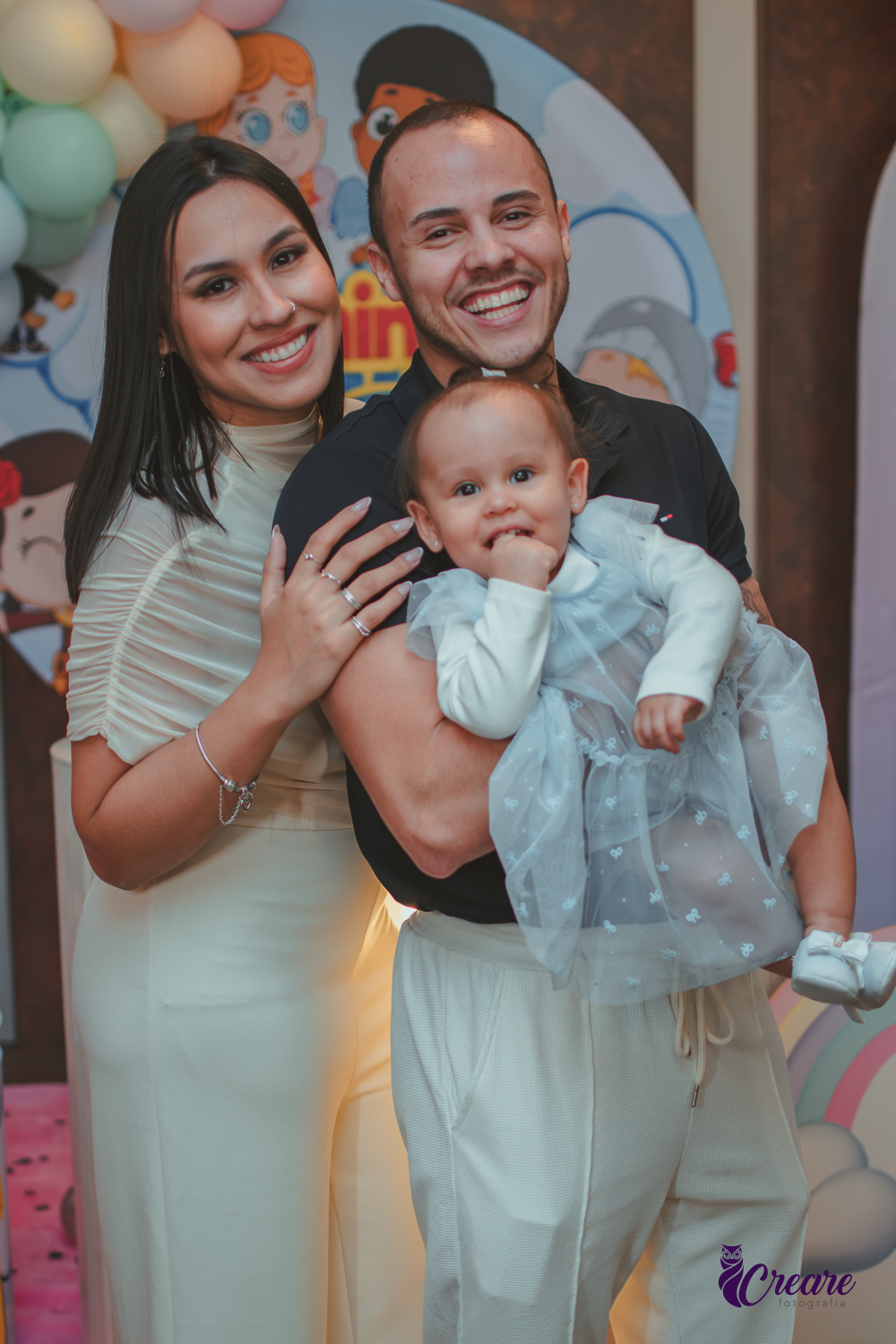 Uma família sorrindo em frente mesa de decoração, na festa de 1 ano da bebê.