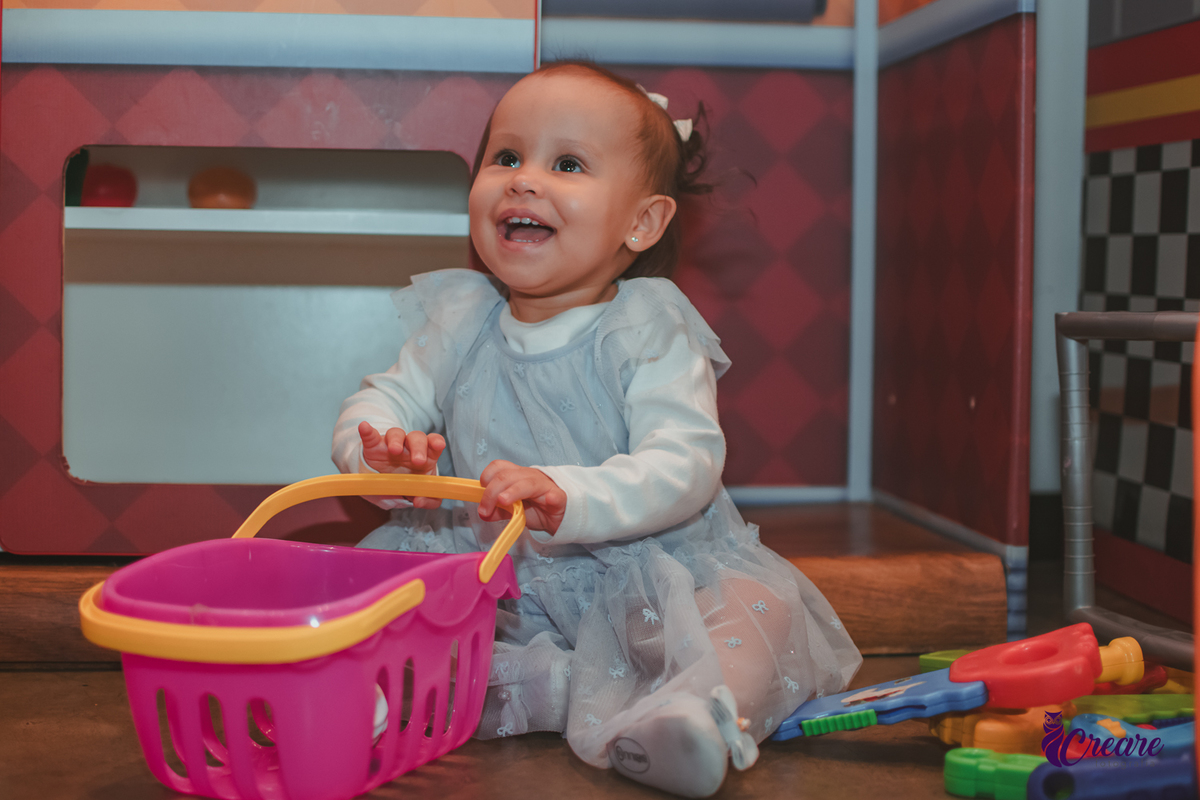 Uma bebê brincando com carrinho rosa em sua festa de aniversário de 1 ano.