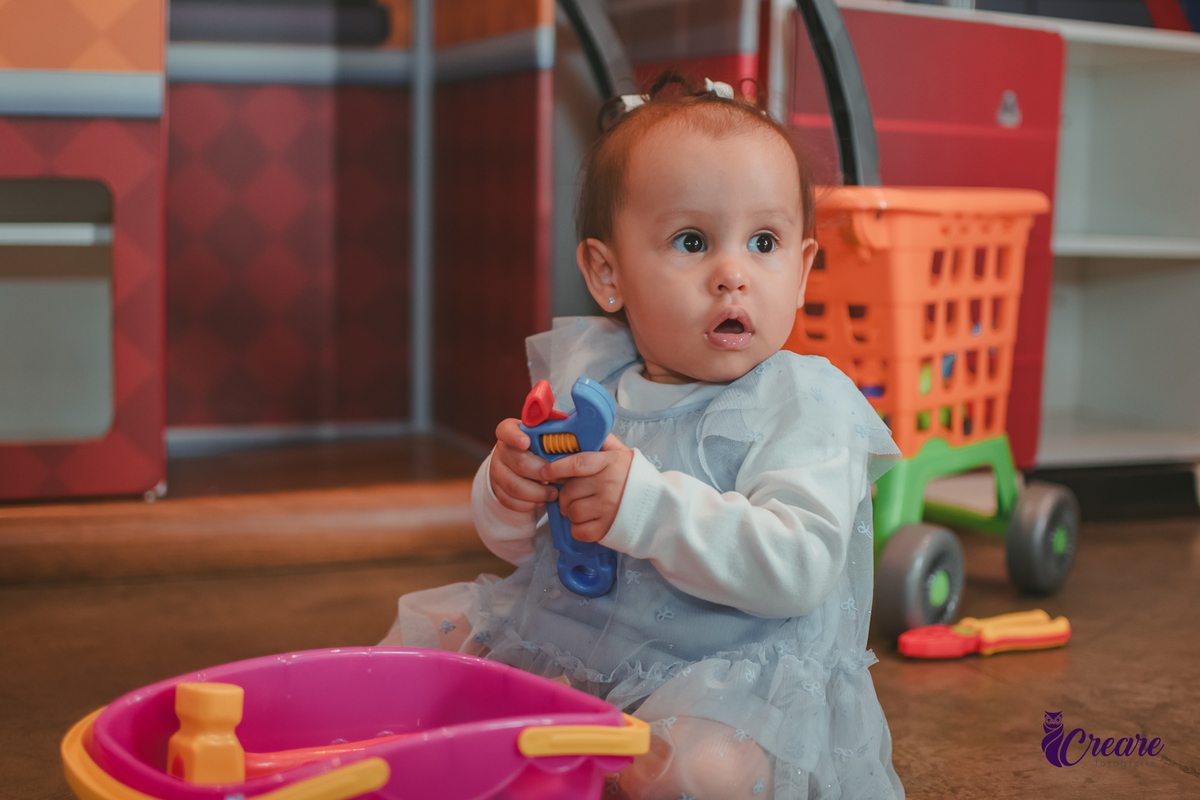 Uma bebê brincando com carrinho rosa em sua festa de aniversário de 1 ano.