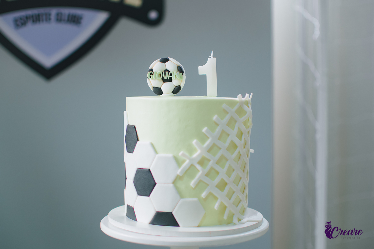 Bolo com decoração de futebolna cor verde e uma vela com número 1 em cima. 