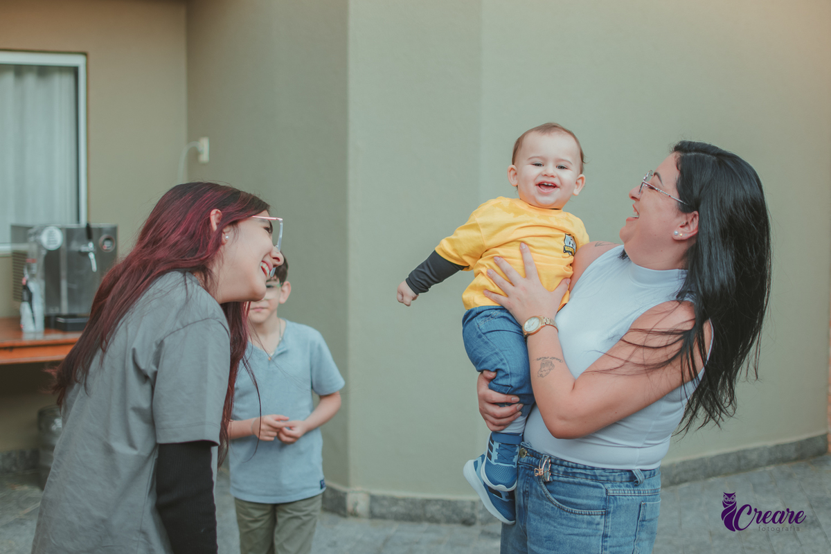 Uma mulher e uma menina brincam com um bebê durante uma festa de aniversário de 1 ano em casa.