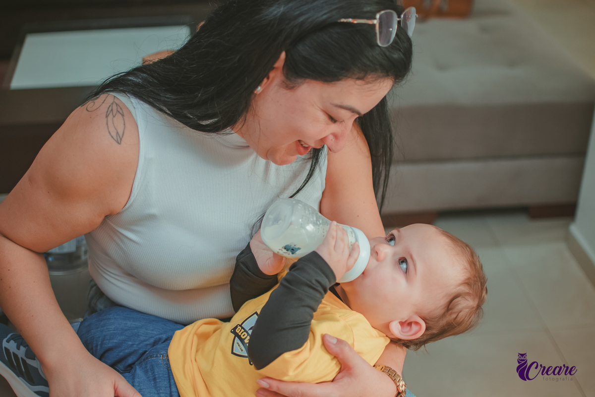 Uma mulher dando mamadeira para um bebê durante seu aniversário de 1 aninho em casa.